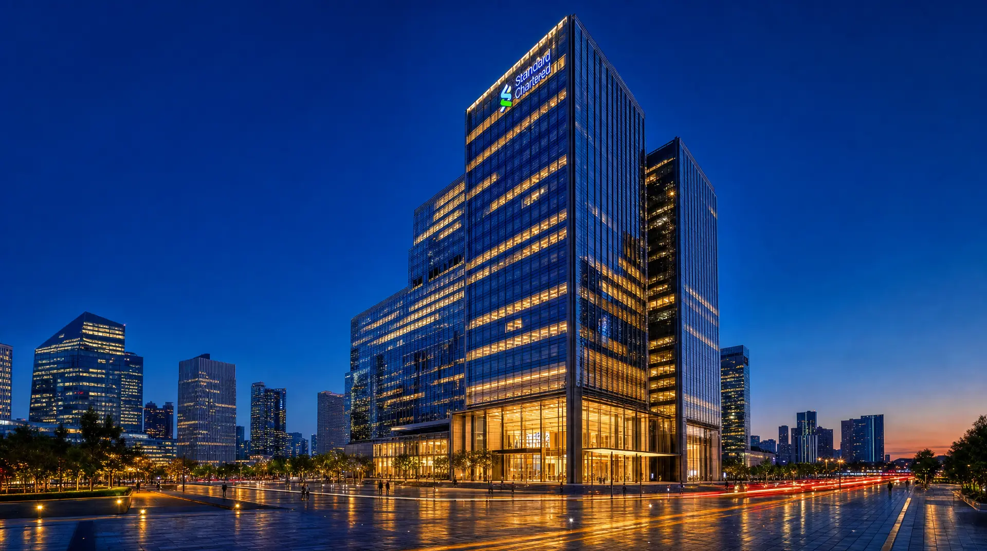 Evening view of a modern office tower with the "Standard Chartered" logo above the entrance, representing corporate banking operations.