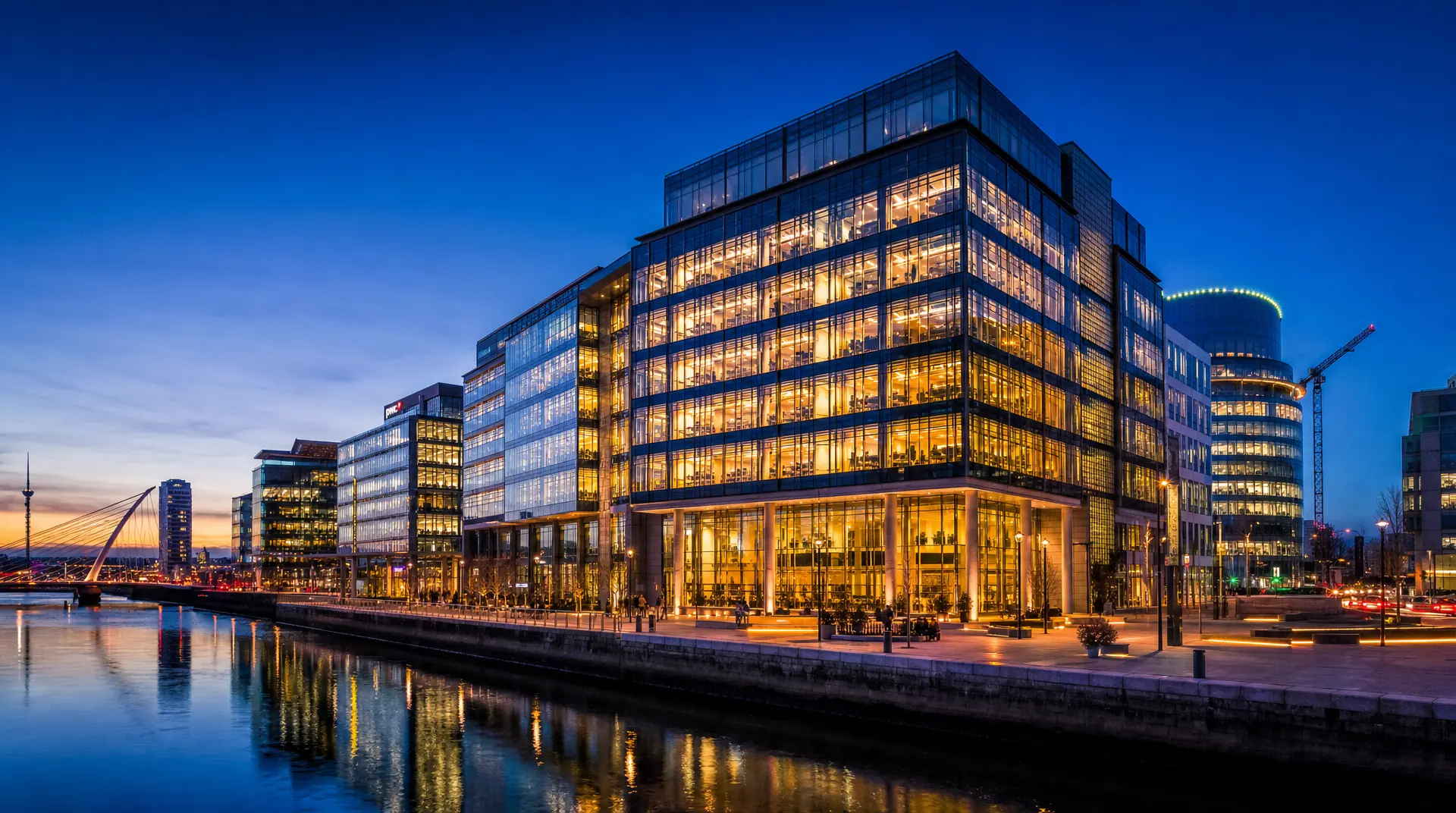 Illuminated glass office complex by a canal at dusk, signaling corporate compliance readiness for global expansion planning.